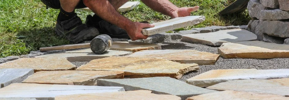 Person verlegt Steinplatten mit Gummihammer